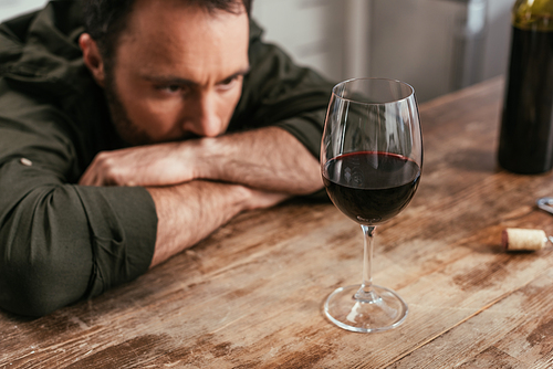 Selective focus of pensive man looking at wine glass on table