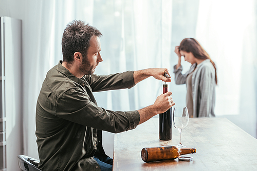 Selective focus of man opening wine bottle and worried woman at home