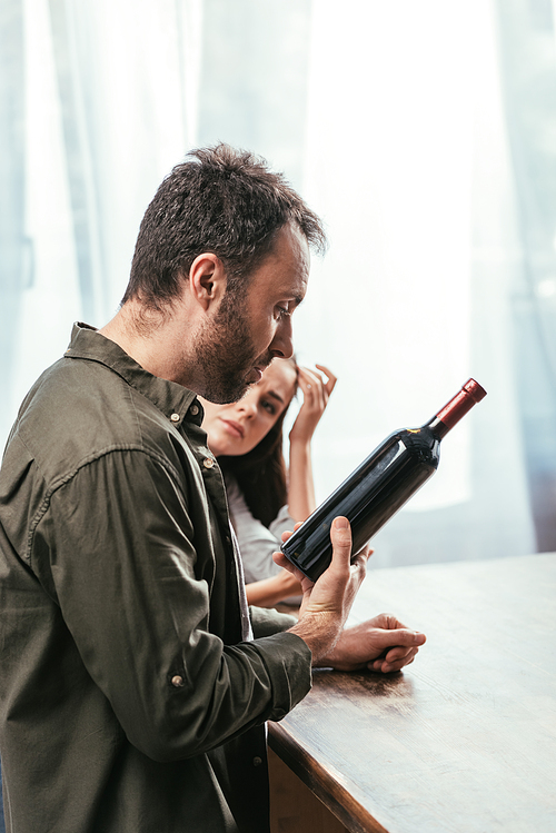 Selective focus of man with wine bottle and worried wife at home