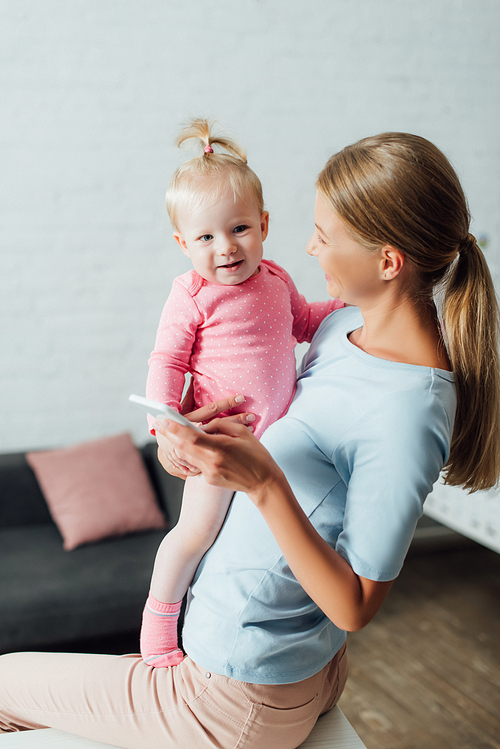 Selective focus of woman holding smartphone and baby girl at home