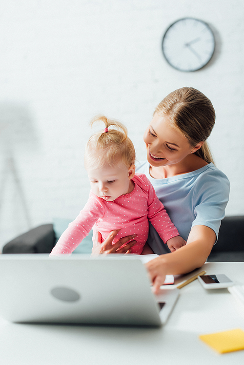 Selective focus of mother holding baby girl near gadgets on table