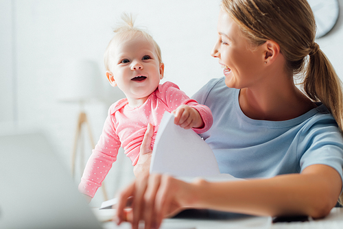 Selective focus of infant girl holding notebook near mother at home