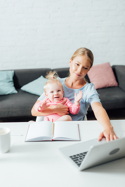 Selective focus of freelancer working on laptop and holding infant daughter at table