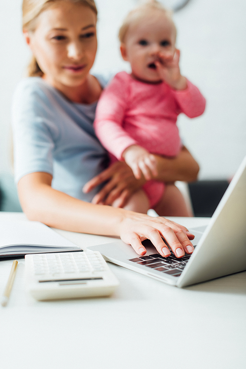 Selective focus of teleworker using laptop while holding baby girl at table