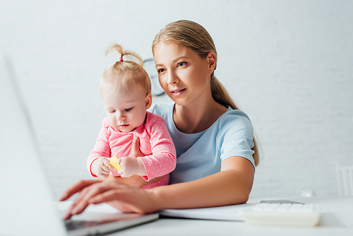 Selective focus of freelancer using laptop while holding baby daughter at table