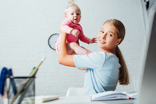 Selective focus of woman looking at laptop while playing with infant daughter at home