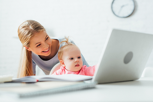 Selective focus of mother standing near kid looking at laptop and stationery on table