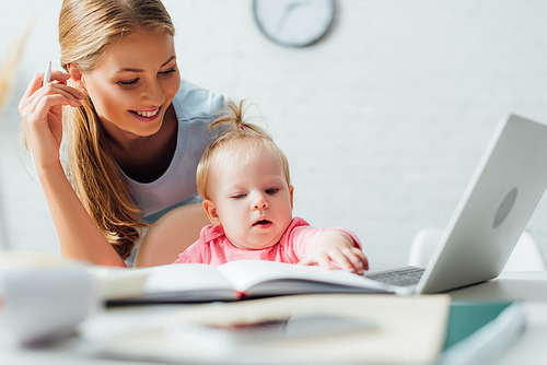 Selective focus of infant touching notebook near laptop and mother at home