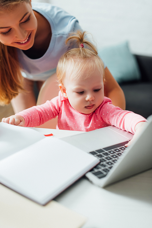 Selective focus of infant touching laptop near mother at home