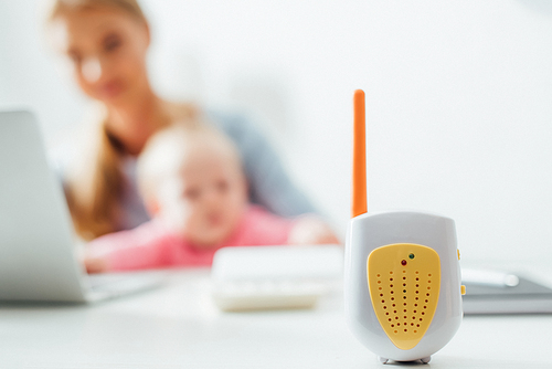 Selective focus of baby monitor on table and mother with infant using laptop at table