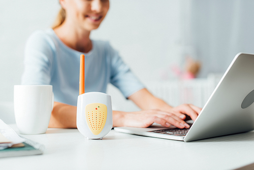 Selective focus of baby monitor on table near woman using laptop at home