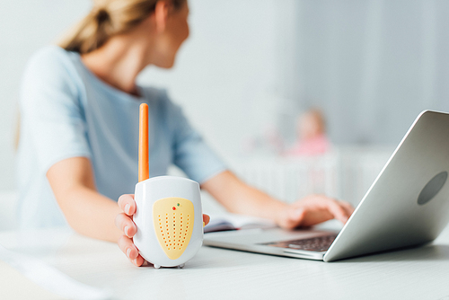 Selective focus of woman using laptop and holding baby monitor at home