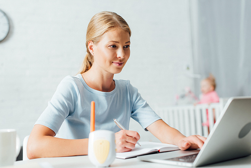 Selective focus of woman working with laptop and notebook near baby monitor on table