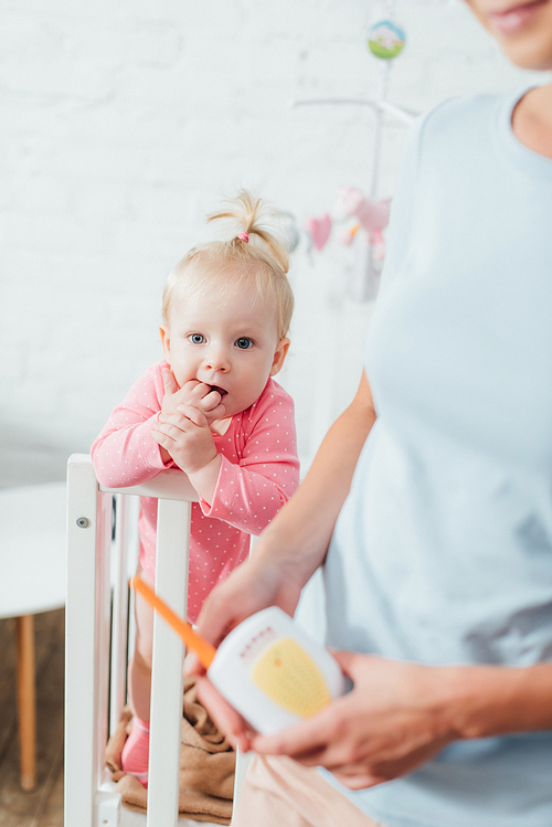 Selective focus of infant in crib near mother holding baby monitor