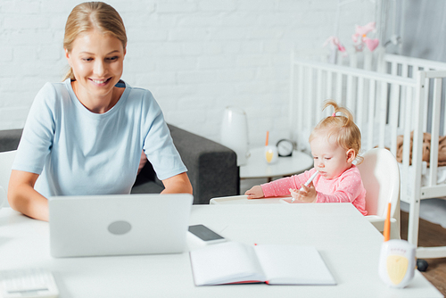 Selective focus of baby girl holding pen while mother using laptop at home