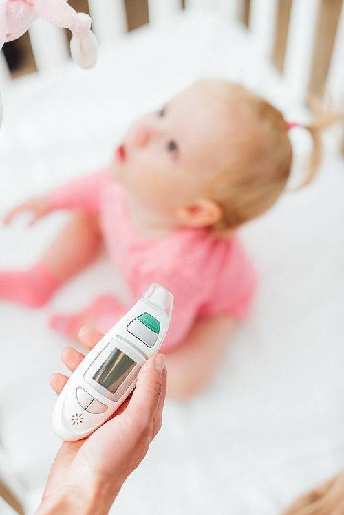 Selective focus of mother holding inhaler near baby girl in crib