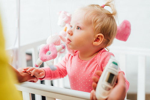 Selective focus of infant girl in crib near mother holding electronic inhaler