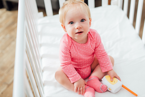 Selective focus of infant girl holding baby monitor while sitting in crib