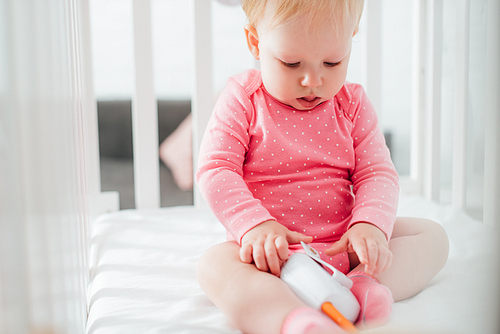 Selective focus of infant girl holding baby monitor in crib