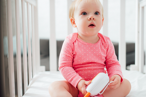 Selective focus of excited infant holding baby monitor in crib