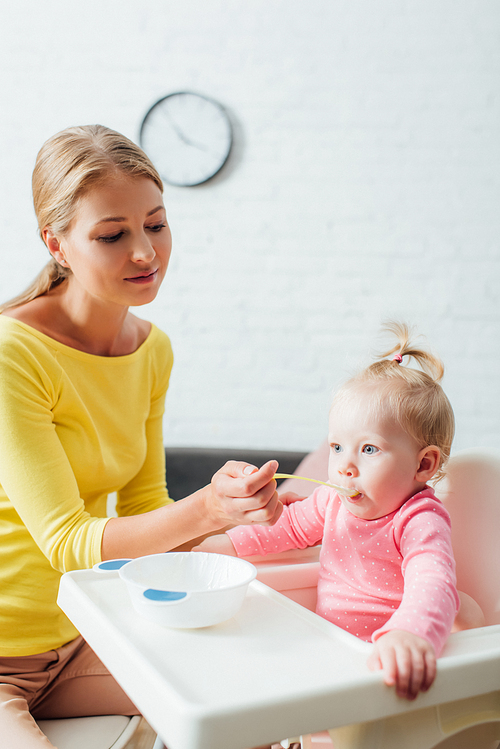 Selective focus of mother with spoon feeding infant daughter on highchair