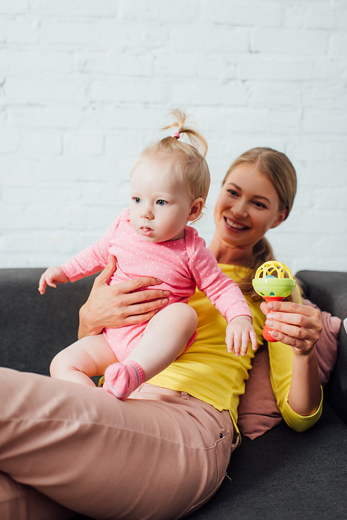 Selective focus of woman holding toy and infant daughter on couch