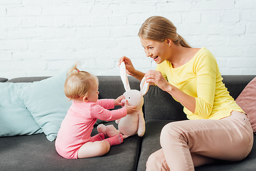 Mother and baby girl playing with soft toy on couch