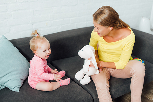 Woman holding soft toy while playing with baby daughter in living room