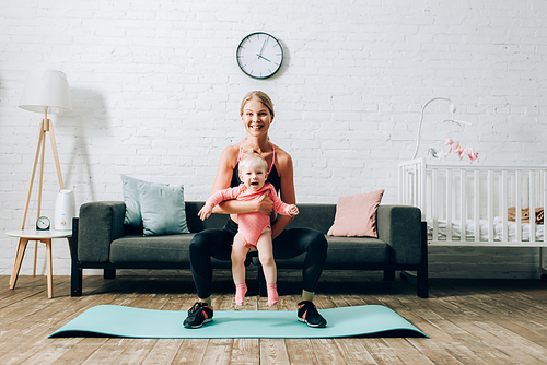 Sportswoman embracing infant daughter while training on fitness mat in living room