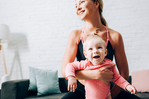 Mother in sportswear holding baby girl at home