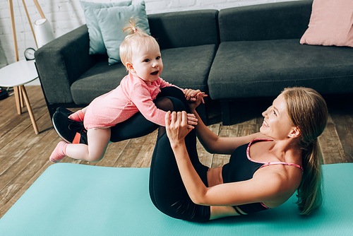 Sportswoman holding baby daughter while working out on fitness mat at home