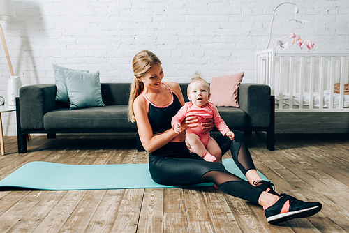 Sportswoman hugging baby girl while sitting on fitness mat at home