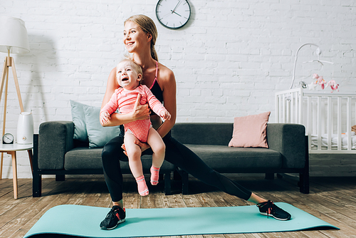 Woman training on fitness mat and holding baby daughter at home