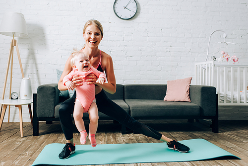 Sportswoman doing lunges on fitness mat and carrying baby daughter