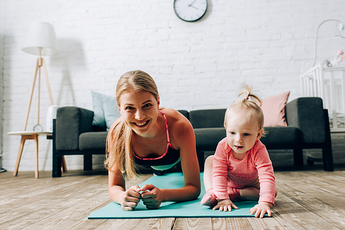 Sportswoman doing plank near child on fitness mat