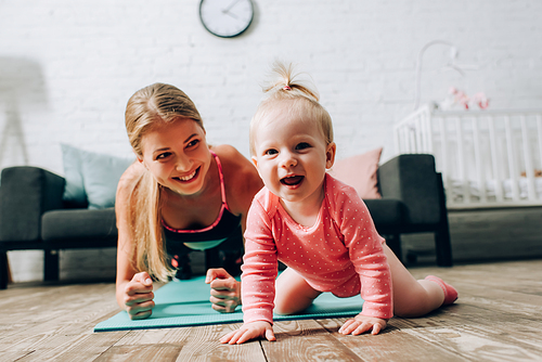 Selective focus of child  near mother doing plank on fitness mat at home