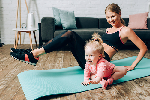 Selective focus of baby girl sitting on fitness mat while mother training at home