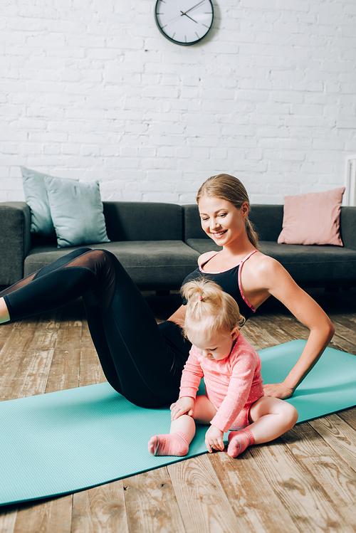 Selective focus of baby girl sitting on fitness mat while mother training at home