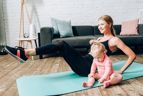 Selective focus of woman training on fitness mat near baby daughter in living room