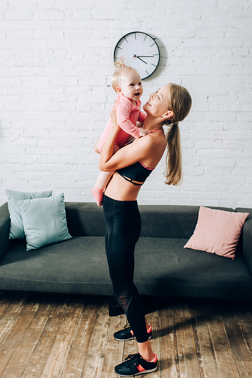 Mother in sportswear and sneakers holding infant girl at home