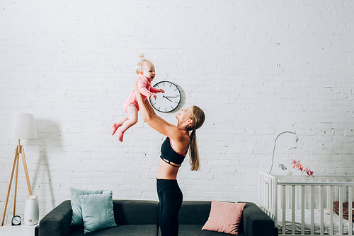 Side view of mother in sportswear holding daughter at home