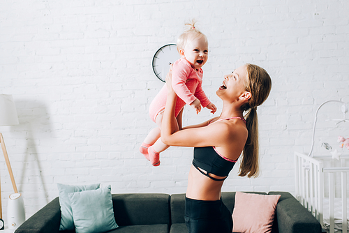 Woman in sportswear holding infant girl in living room