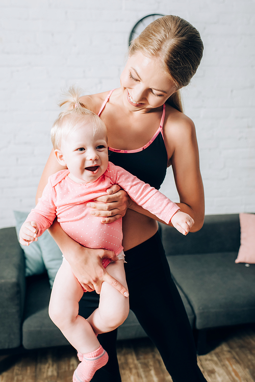 Mother in sportswear holding baby girl in living room