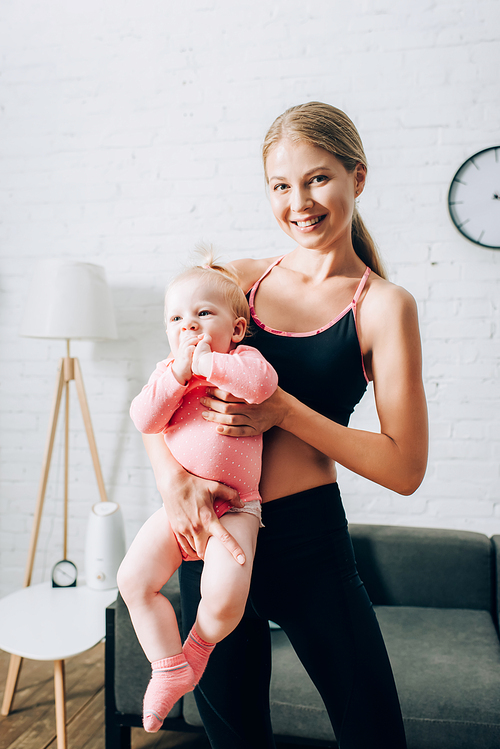 Fit woman in sportswear holding infant child in living room