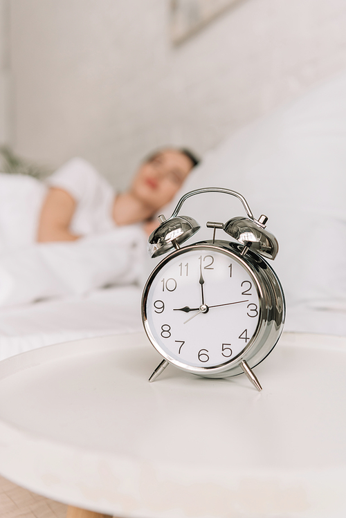 selective focus of vintage alarm clock on white bedside table and sleeping girl on background