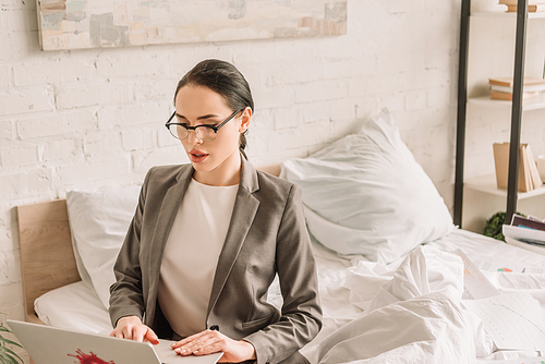 beautiful businesswoman in blazer over pajamas using laptop in bedroom