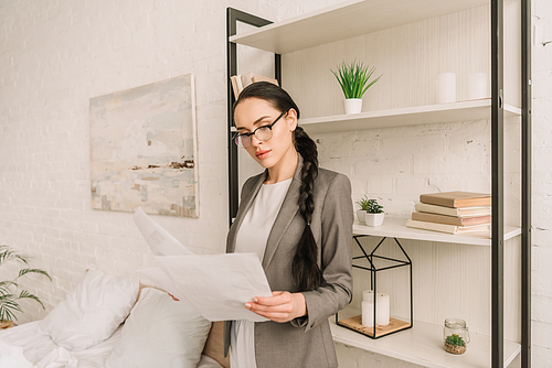 attentive businesswoman in blazer over pajamas  while standing in bedroom