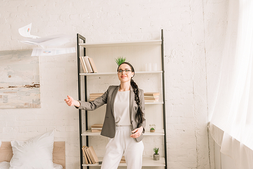 happy businesswoman in blazer over pajamas throwing up documents while  in bedroom