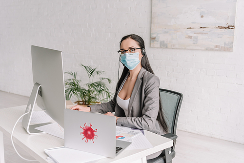 businesswoman in medical mask and headset  while working at home near laptop and computer monitor