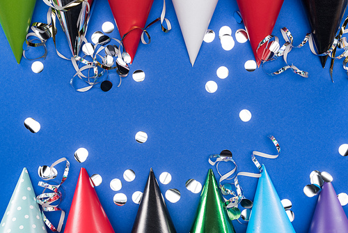 Top view of party hats and silver confetti on blue background